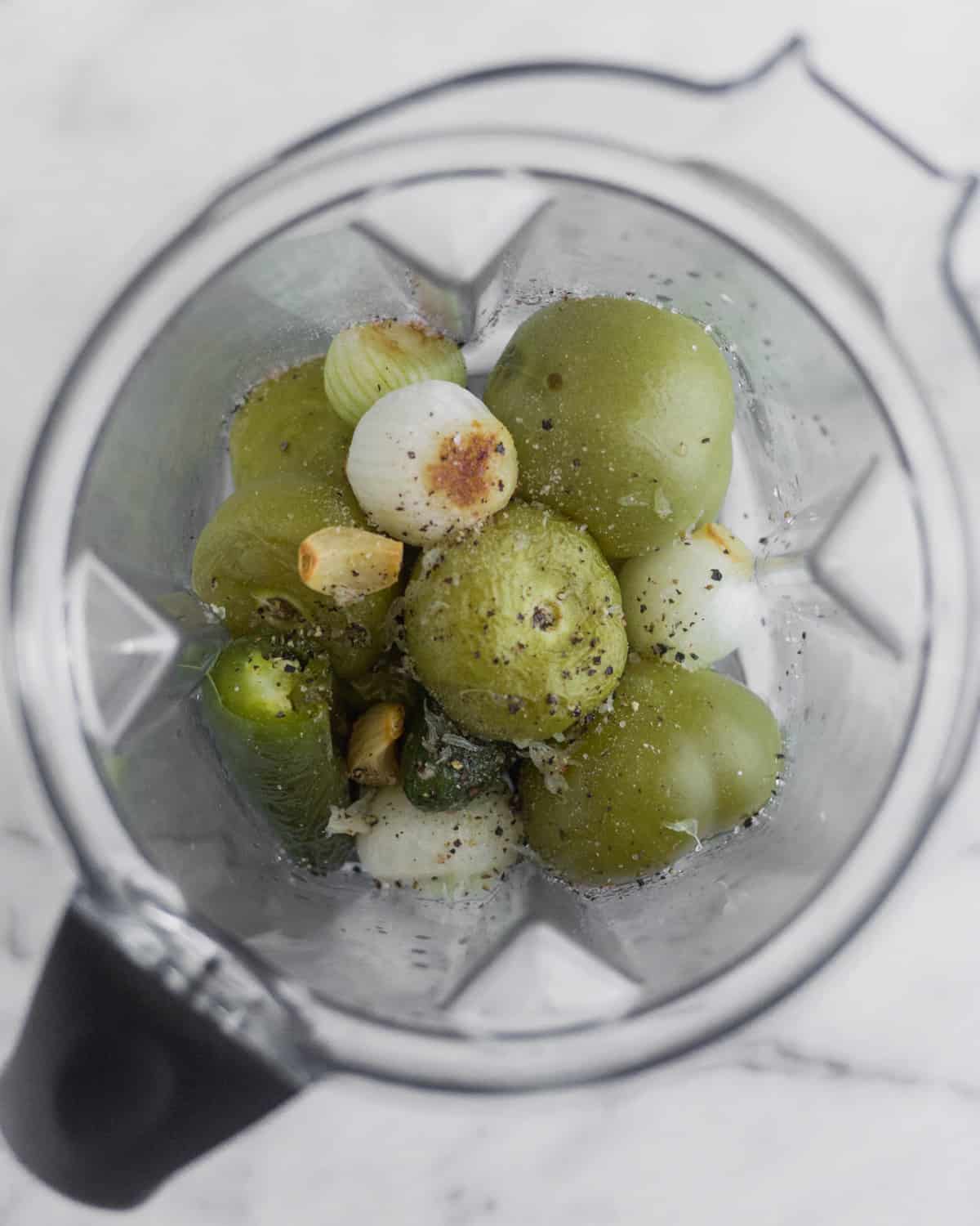 Blender filled with roasted tomatillos, onions, jalapeños, and garlic