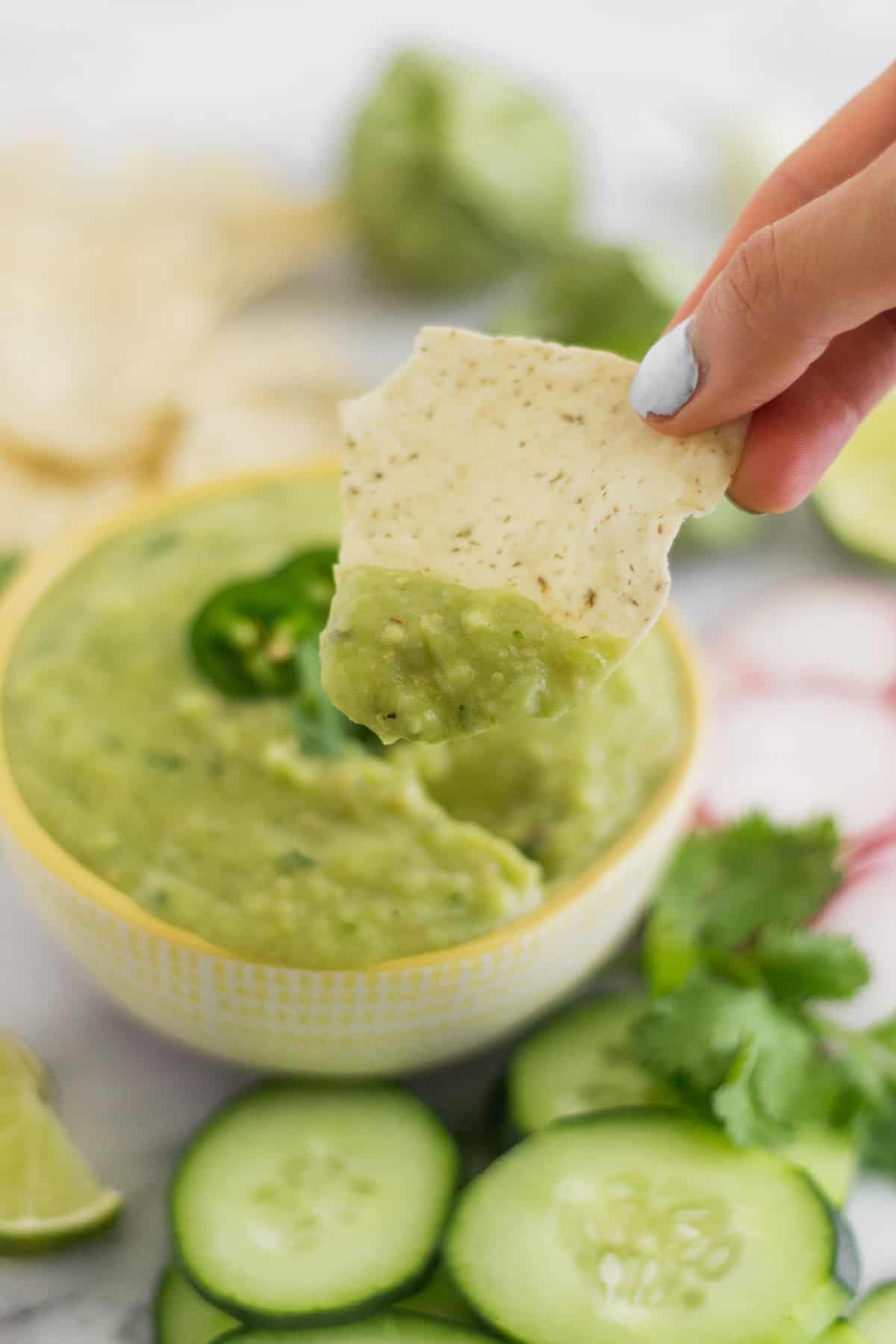 A hand dipping a chip into a bowl of Roasted Tomatillo Avocado Salsa