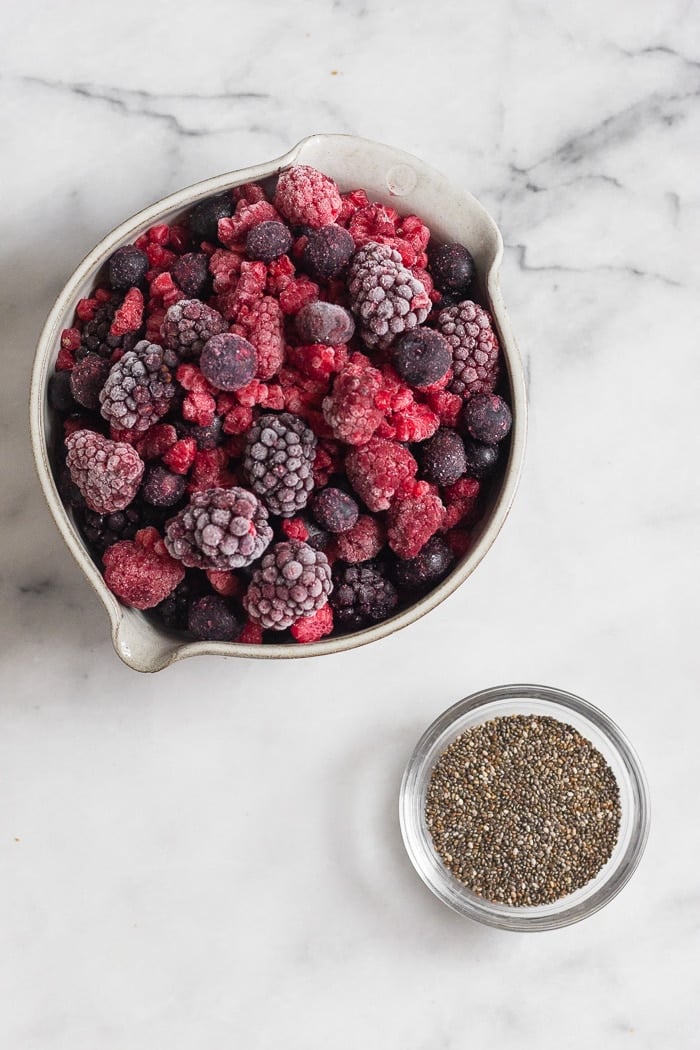 Bowl of mixed frozen berries and a small bowl of chia seeds on a white counter top.