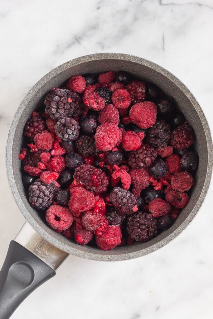 A small saucepan filled with frozen blackberries, blueberries, and raspberries.