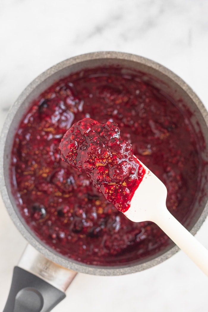 Overhead shot of a chia seed jam with a spatula overtop with a scoop of it on it.