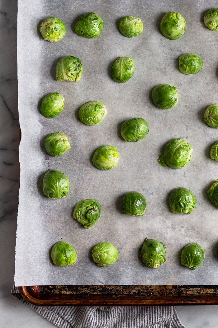 Baking sheet lined with parchment paper with halved brussel sprouts facing cut side down.