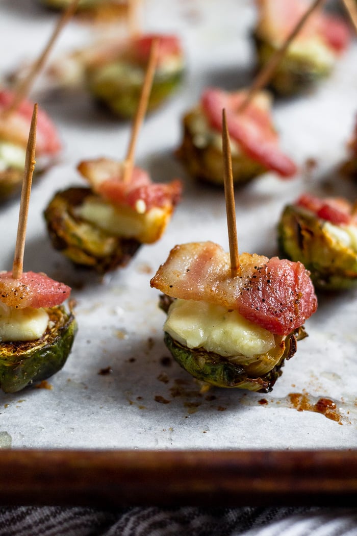A bunch of halved brussel sprouts that have been roasted and topped with blue cheese and crispy bacon. A toothpick is stuck in each one.