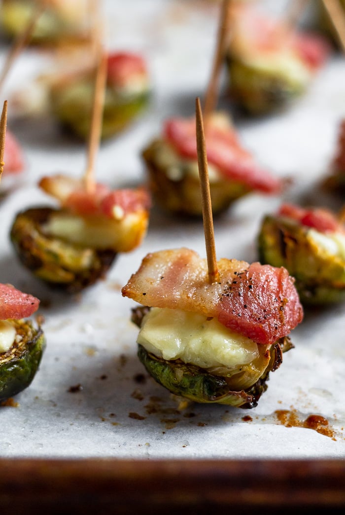 Individual halved roasted brussel sprouts topped with blue cheese and bacon with a toothpick stuck in them.