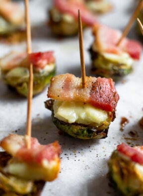 Individual crispy brussel sprouts with bacon and cheese with a toothpick stuck in each one.