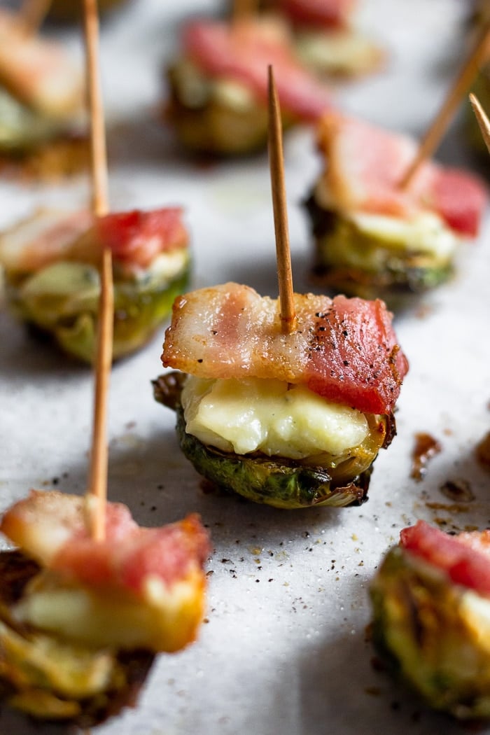 Individual crispy brussel sprouts with bacon and cheese with a toothpick stuck in each one.