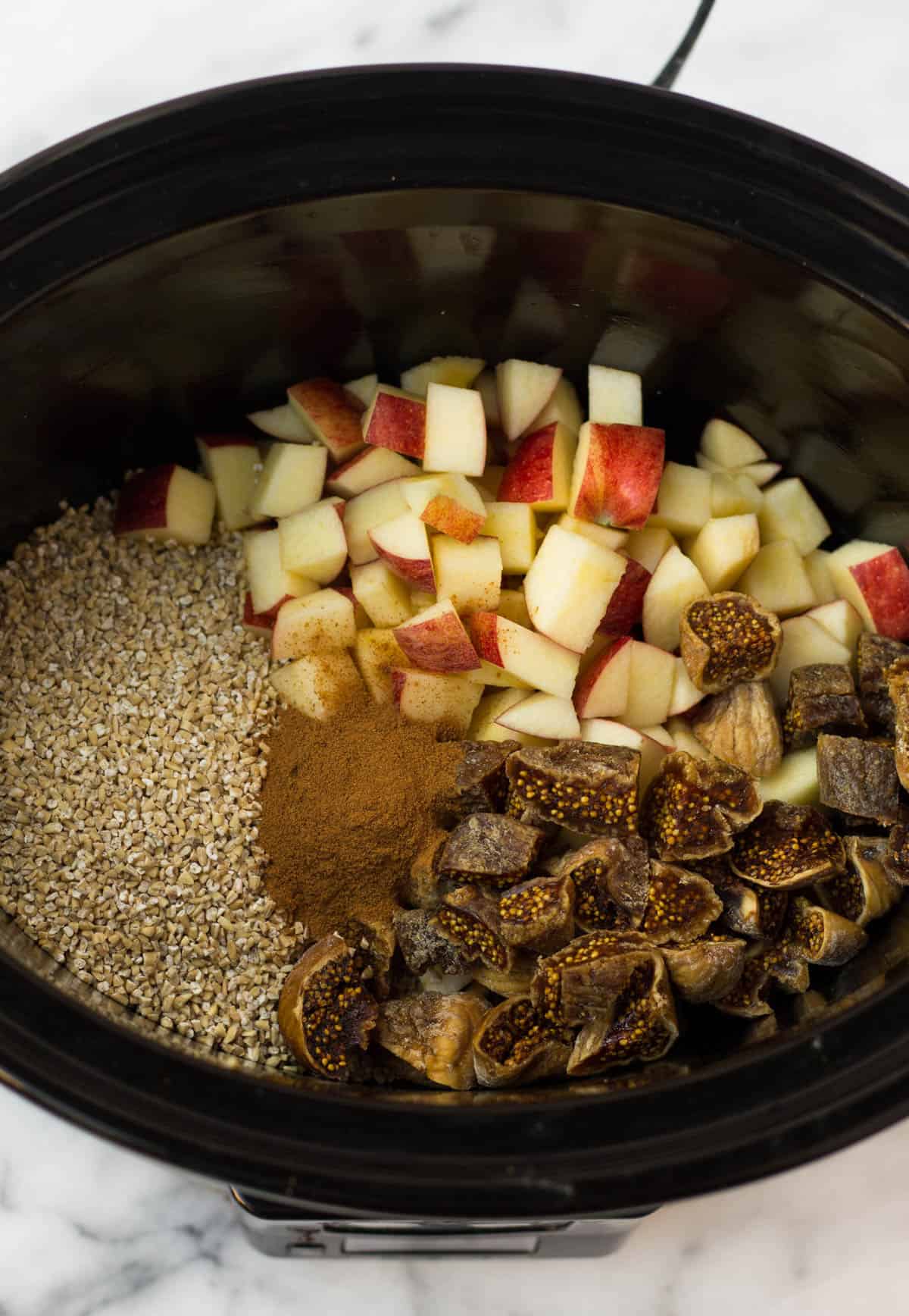 Crockpot filled with steel cut oats, diced apples, dried figs, and cinnamon.