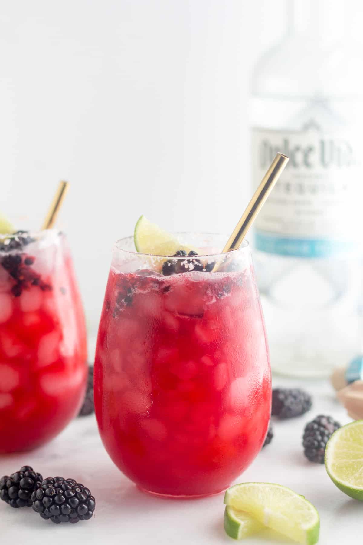 A glass filled with a healthy margarita. Behind it is another margarita and a bottle of tequila.