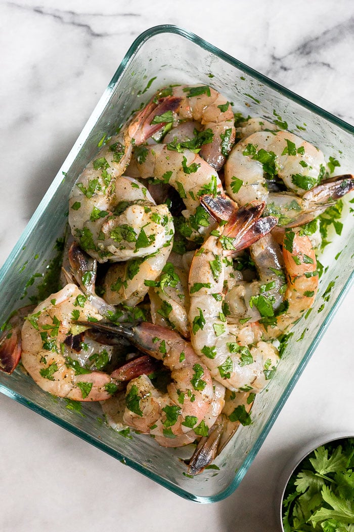 Glass dish filled with raw shrimp and cilantro lime shrimp marinade.