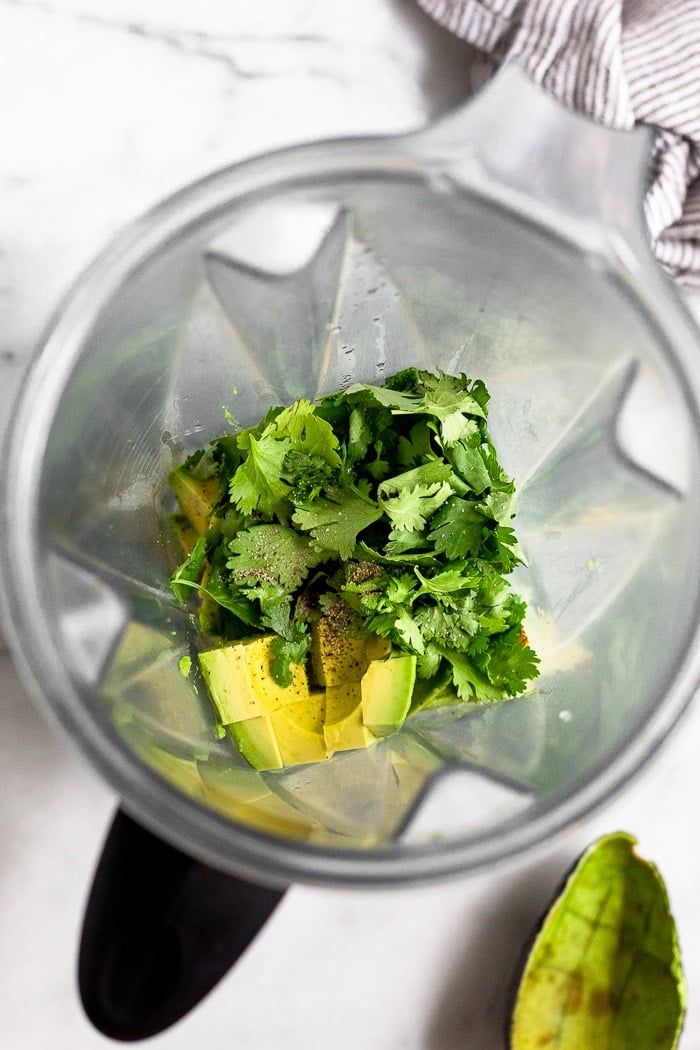 Blender filled with avocado, cilantro, lime juice, and salt and pepper to make avocado sauce.