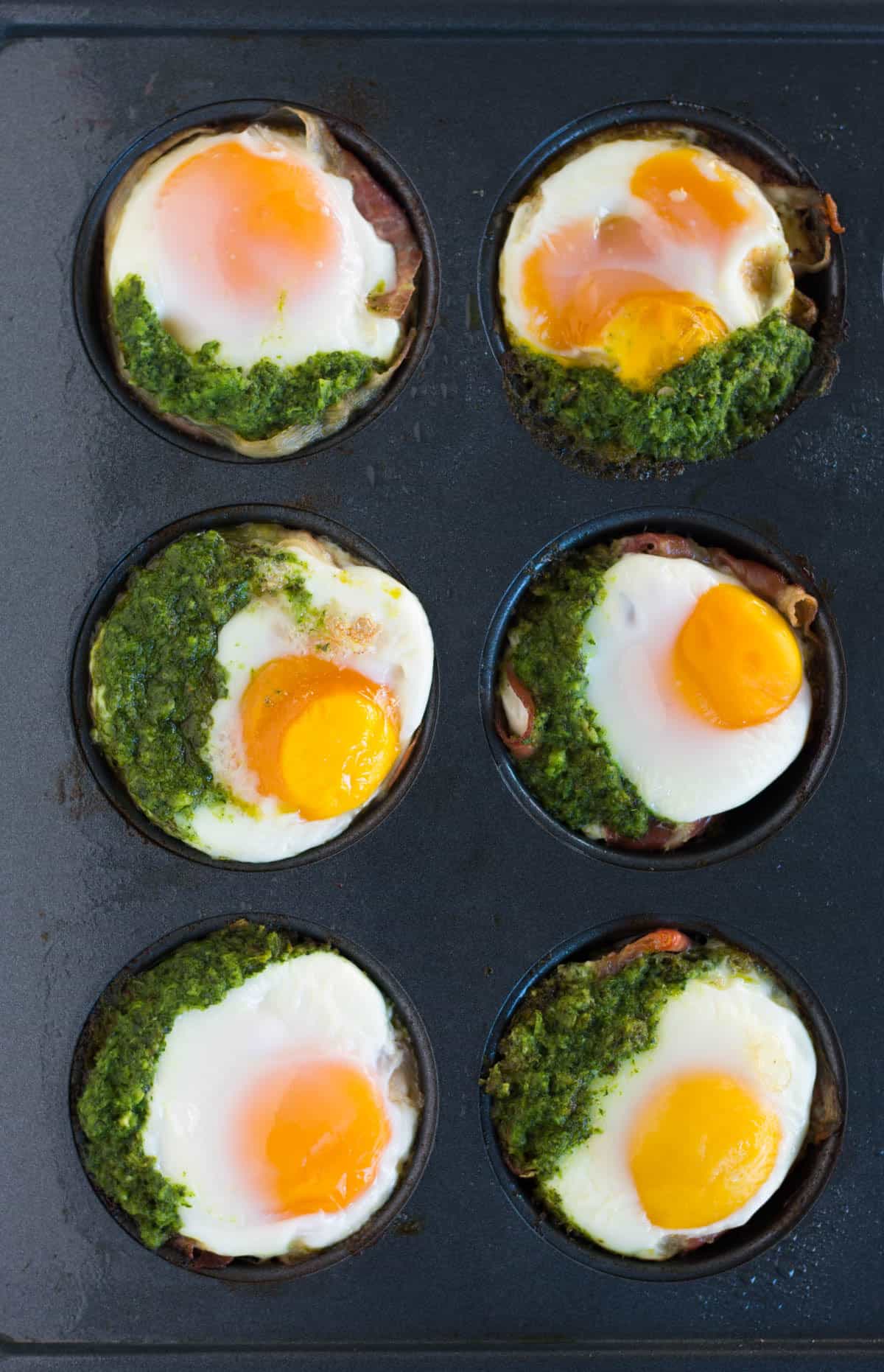 Overhead of 6 prosciutto egg cups with chimichurri in muffin tins