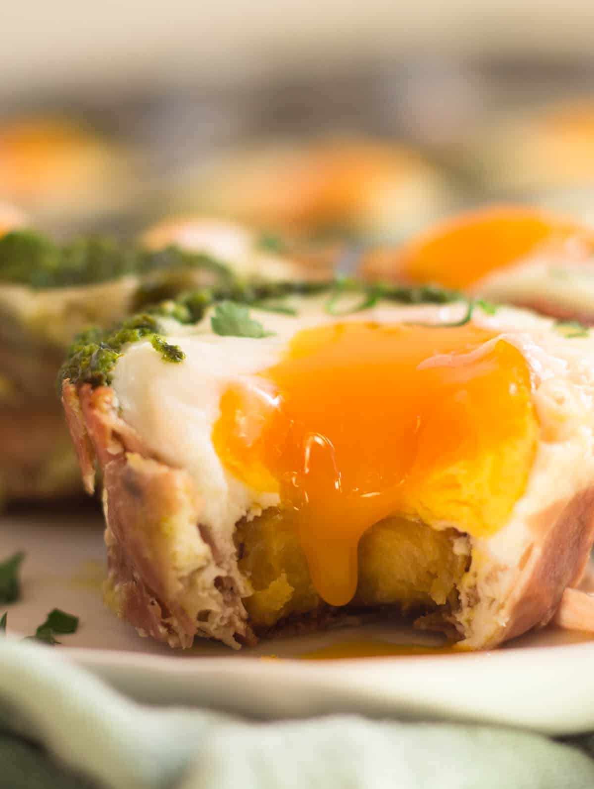 Close up of prosciutto egg cup with a bit taken out of it and the yolk running down
