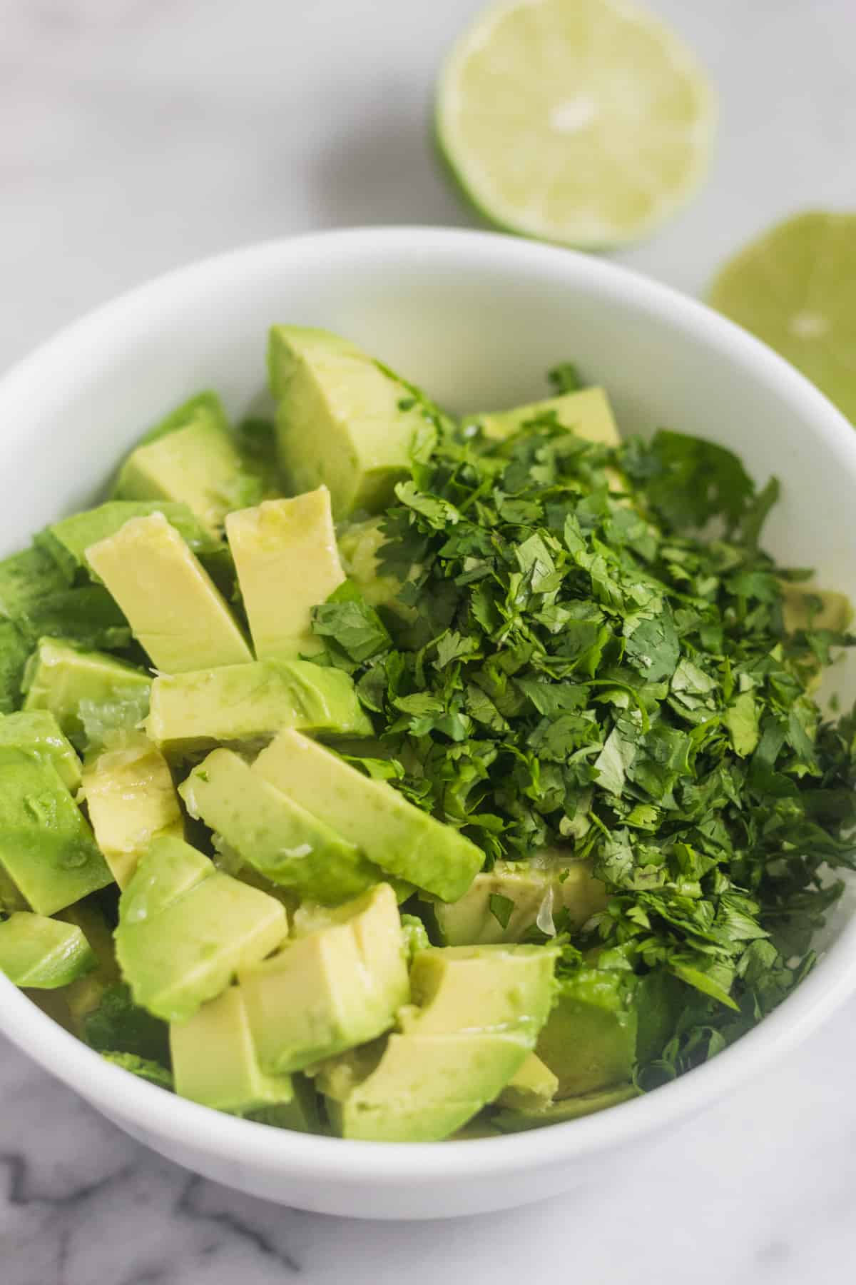 White bowl filled with diced avocado, lime juice, and chopped cilantro