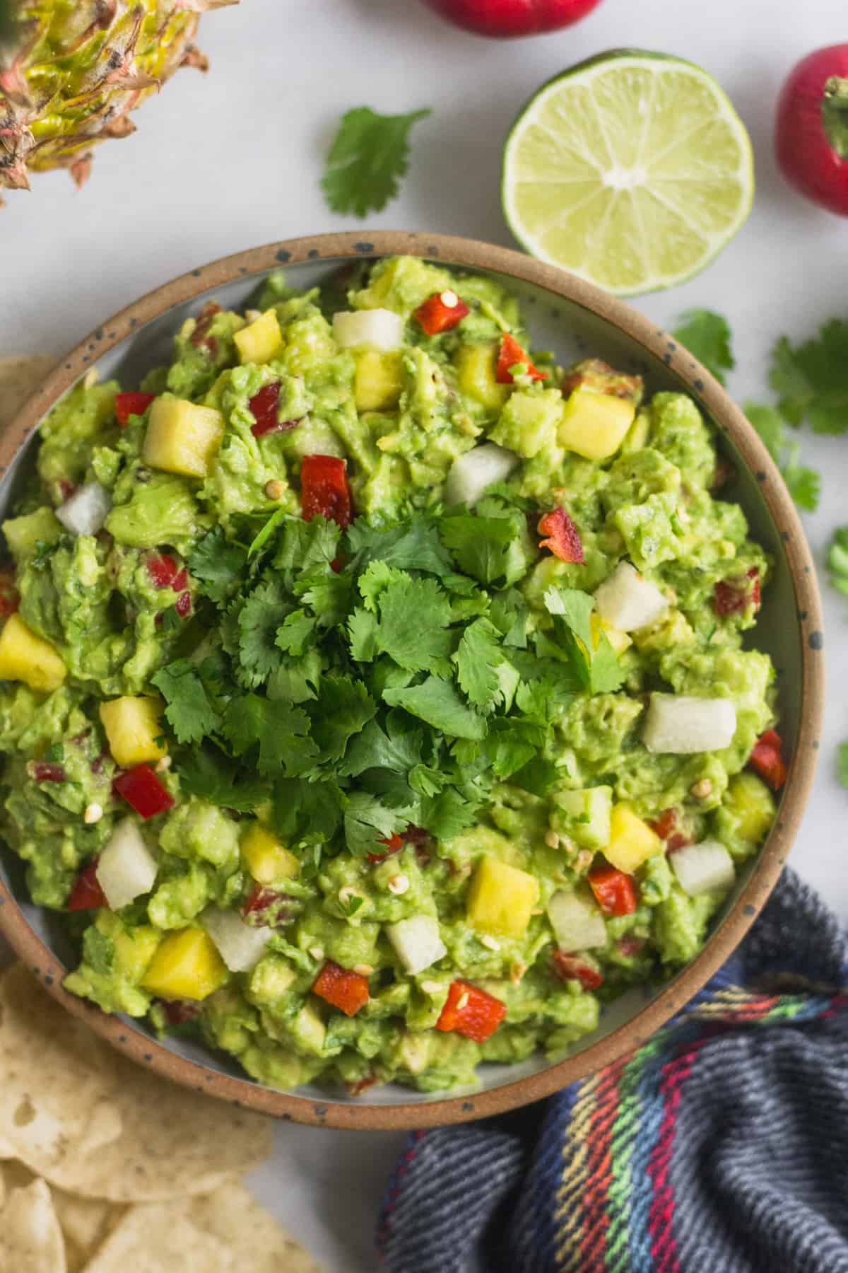 Big bowl of spicy pineapple jicama guacamole surrounded by limes, cilantro, and peppers