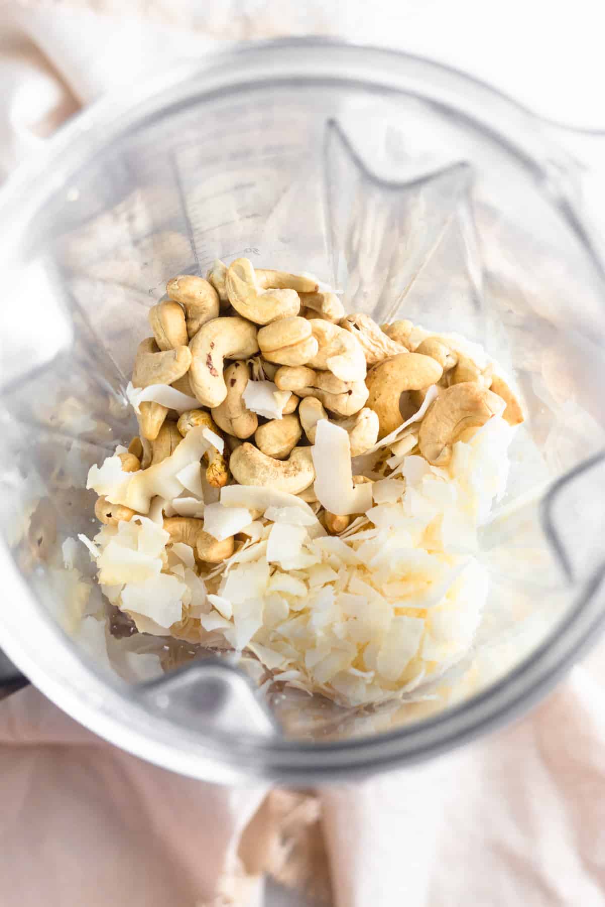 A blender filled with roasted cashews and coconut flakes