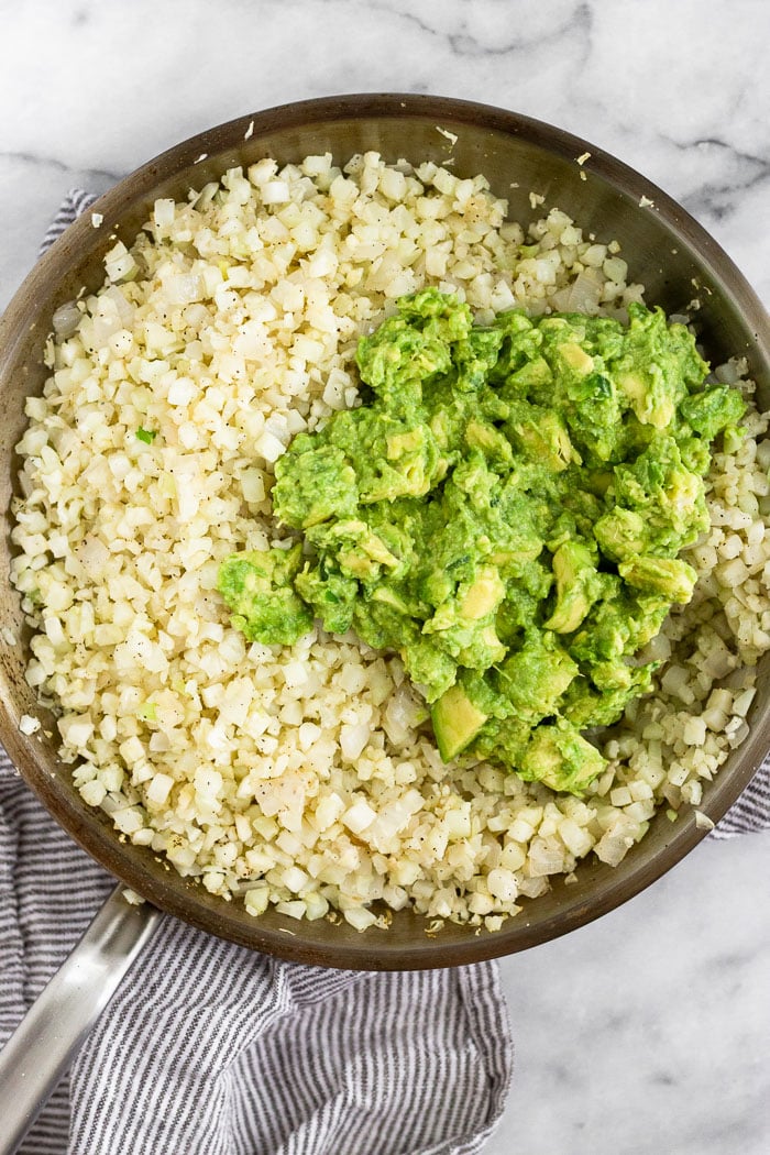 Large pan filled with cook cauliflower rice and a pile of mashed avocado.