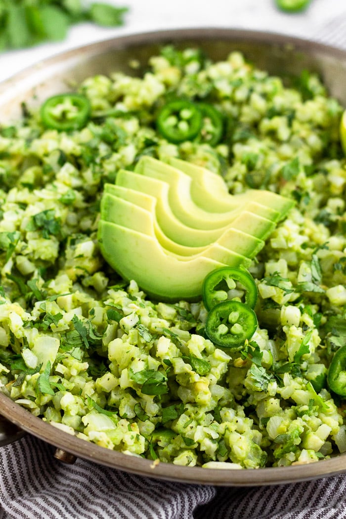 Close up of avocado cauliflower rice in large pan topped with fresh avocado slices and sliced jalapeños.
