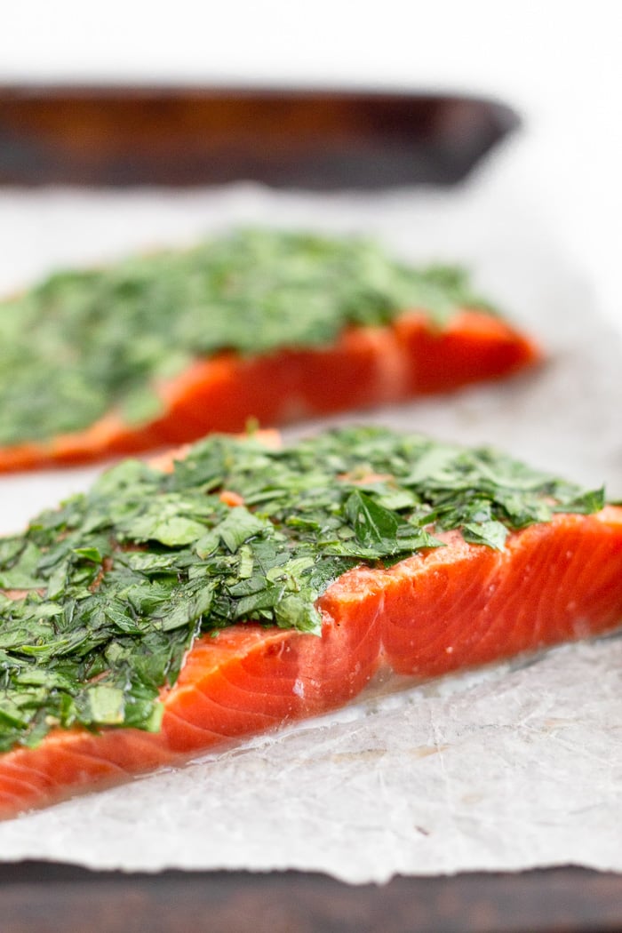 Raw salmon covered with fresh parsley, cilantro, lemon juice, and olive oil on a baking sheet.