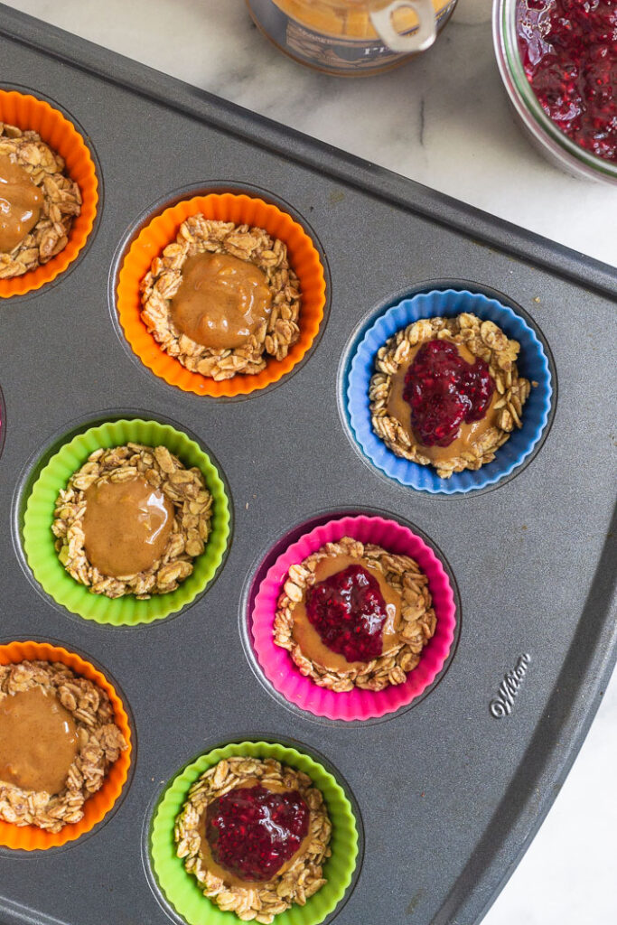 Overhead shot of silicon muffin liners filled with a rolled oat mixture and then layered with peanut butter and jelly.