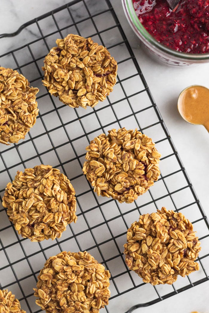 Overhead shot of peanut butter oatmeal muffins on a cooling rack. Next to is a jar of jam and teaspoon of peanut butter.