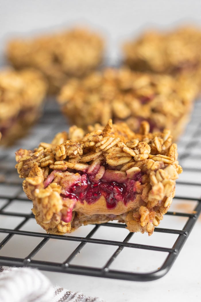 Peanut butter oatmeal muffins on a cooling rack. The closest one has a bite taken out of it with peanut butter and jelly in it.