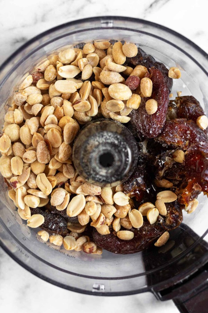 An overhead shot of a food processor container with medjool dates and peanuts in it.