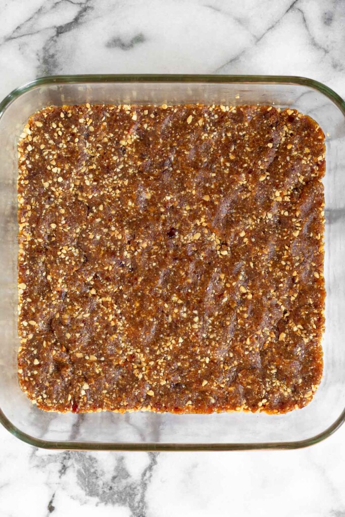 A baking dish with a sticky date and nut mixture pressed into the bottom of the pan.