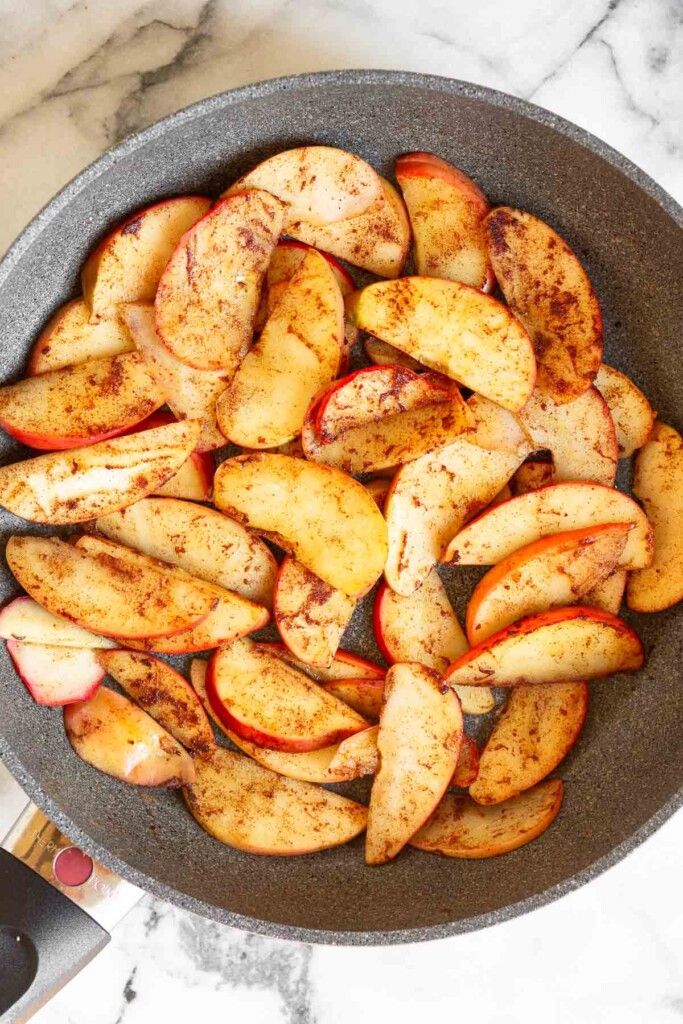 A large skillet filled with sliced sautéed apples with cinnamon on them.