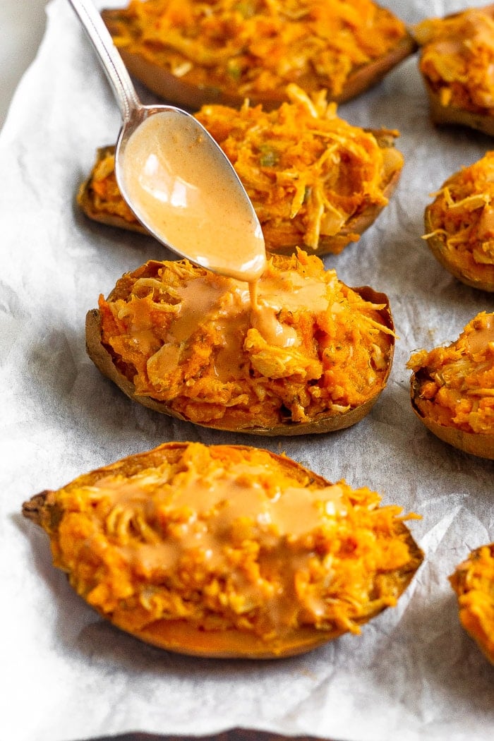 Twice baked stuffed sweet potatoes on a baking sheet being drizzled with sauce.