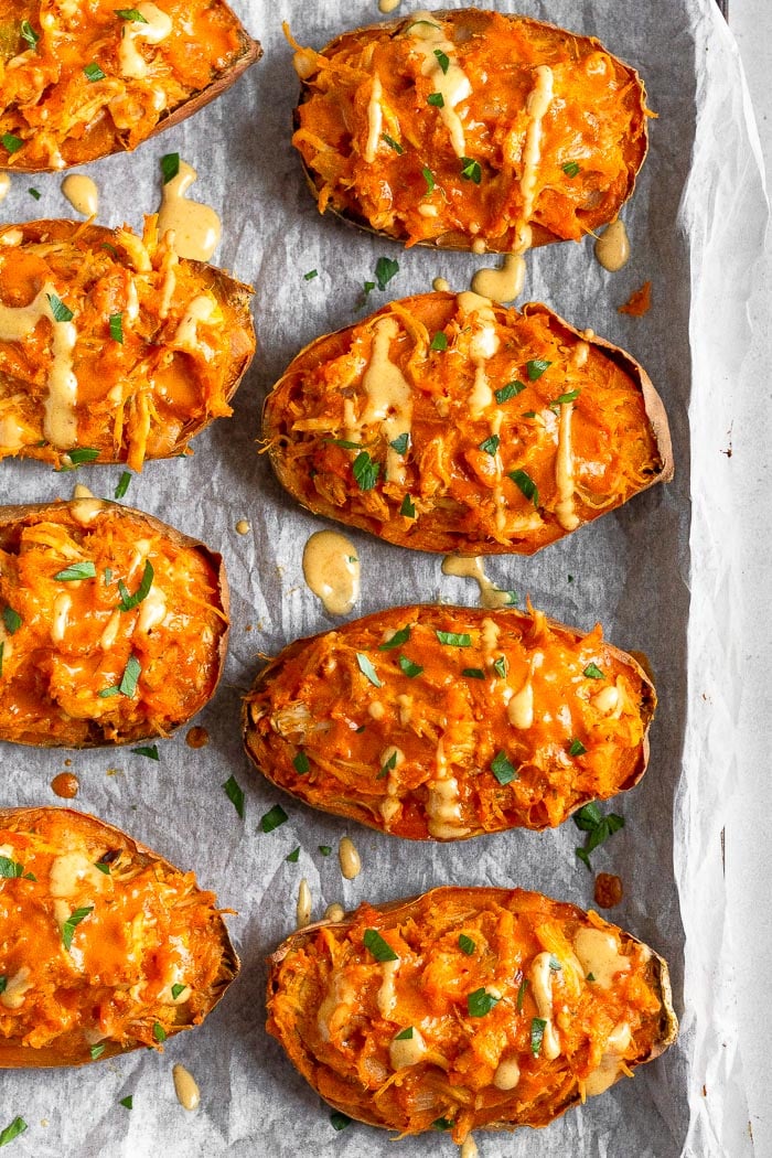 Overhead shot of a bunch of chicken stuffed sweet potatoes drizzled with sauce and topped with fresh herbs on a baking sheet.