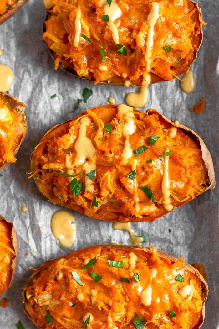 Overhead shot of buffalo chicken sweet potatoes topped with fresh herbs and sauce.