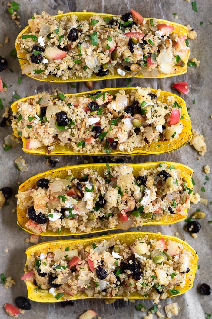 Stuffed delicata squash with quinoa, apple, goat cheese, cranberries, and pumpkin seeds, They are sitting on a baking sheet with some filling that has