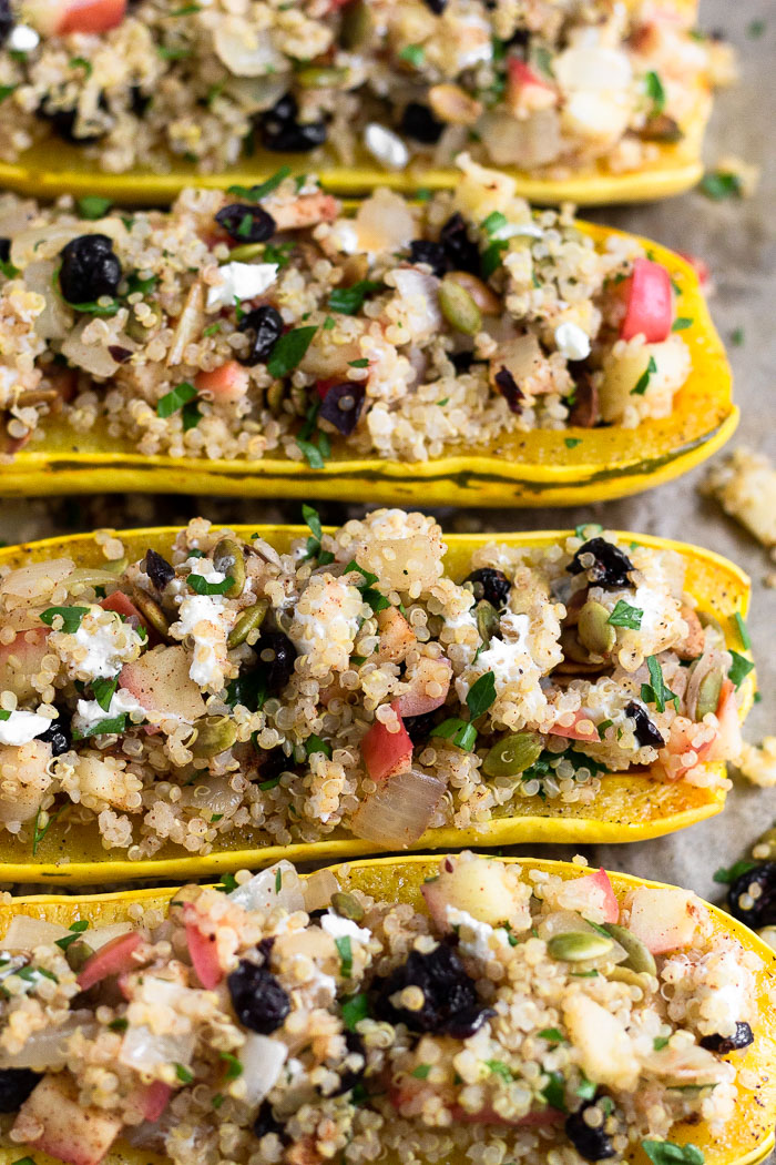 Vegetarian squash stuffed with quinoa, apples, cranberries, goat cheese, and pumpkin seeds lined up next to each other on a baking sheet.