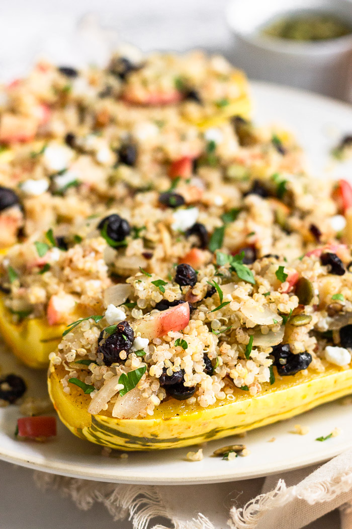 Close up of quinoa stuffed squash on a plate. The quinoa is mixed with apples, cranberries, pumpkin seeds, goat cheese, and parsley.