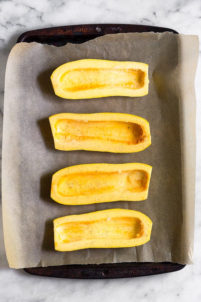 Halved raw delicata squash cut side up on a baking sheet lined with parchment paper.