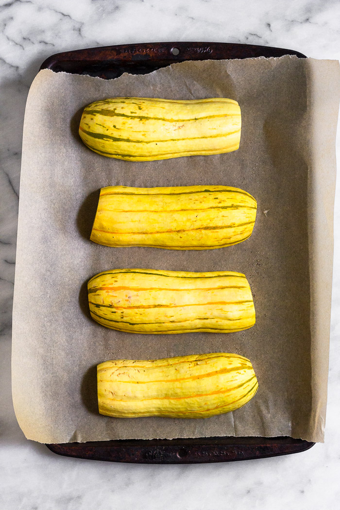 Halved delicata squash cut side down on a baking sheet lined with parchment paper.