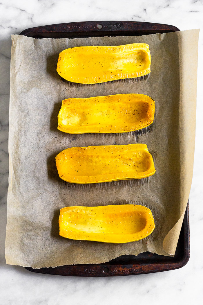 Halved roasted delicata squash cut side up on a baking sheet lined with parchment paper.