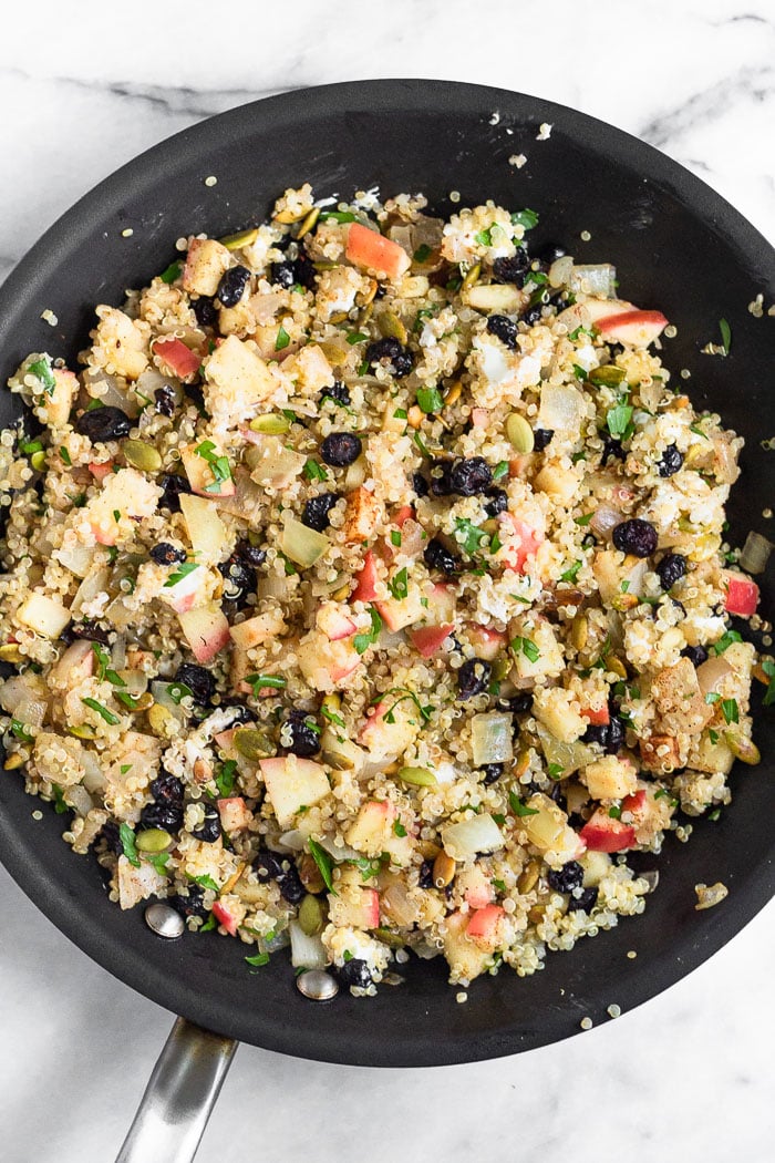 Large saute pan filled with an apple quinoa salad with cranberries, pumpkin seeds, goat cheese, and herbs.