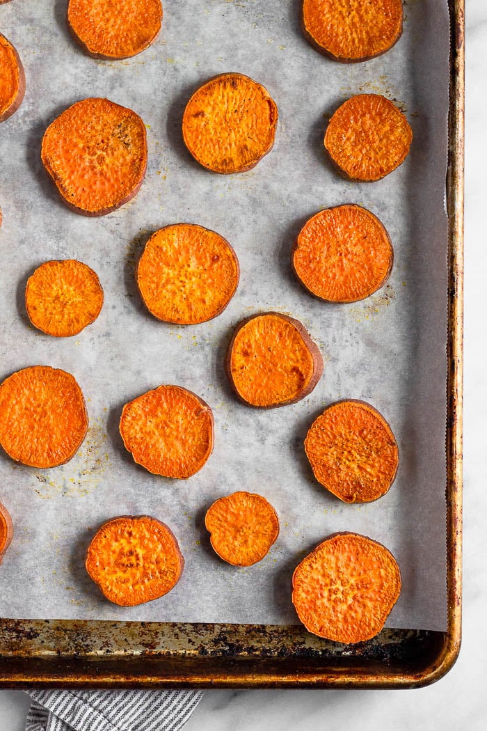 A baking sweet lined with parchment paper with cooked sweet potato rounds on it.