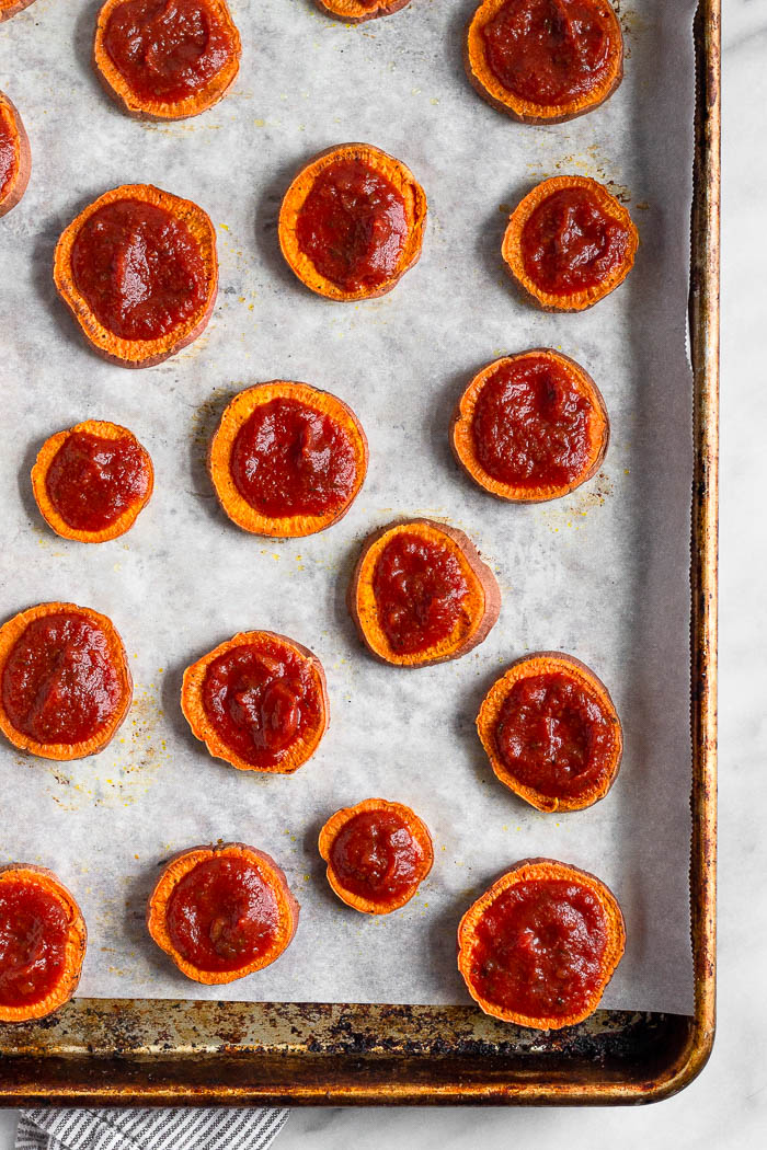 A baking sweet lined with parchment paper with cooked sweet potato rounds topped with sauce.