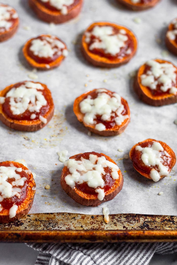 Baking sheet lined with parchment paper with sweet potato rounds topped with sauce and melted cheese.