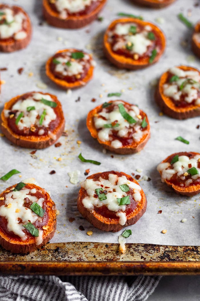 A lot of sweet potato pizza on a baking sheet. They are sprinkled with basil and red pepper flakes.