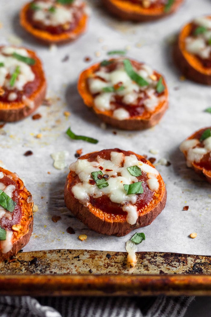 Baking sheet lined with parchment paper with a bunch of mini sweet potato pizzas on it.