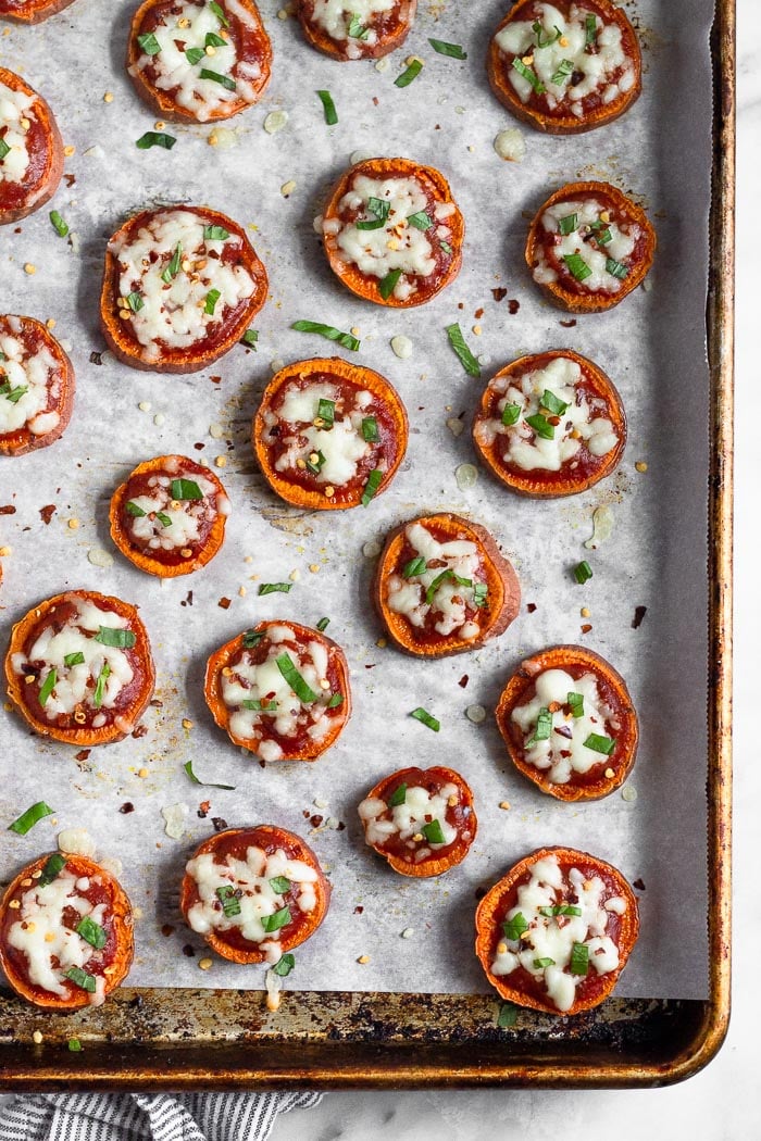 Overhead shot of sweet potato pizzas on a baking sheet topped with chopped basil and red pepper flakes.