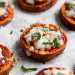Parchment paper lined baking sheet filled with sweet potato pizza rounds topped with basil and red pepper flakes.