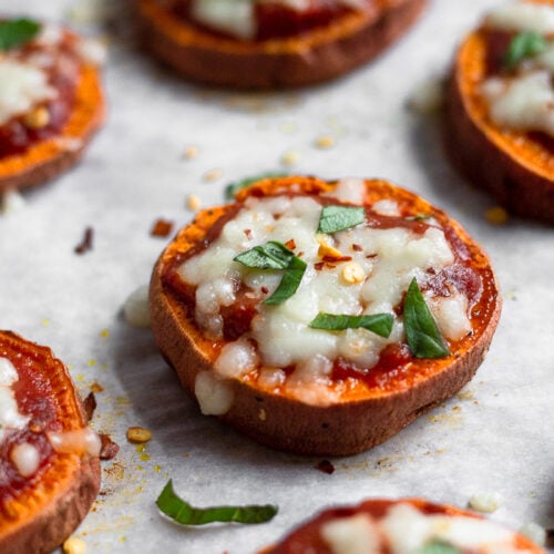 Parchment paper lined baking sheet filled with sweet potato pizza rounds topped with basil and red pepper flakes.