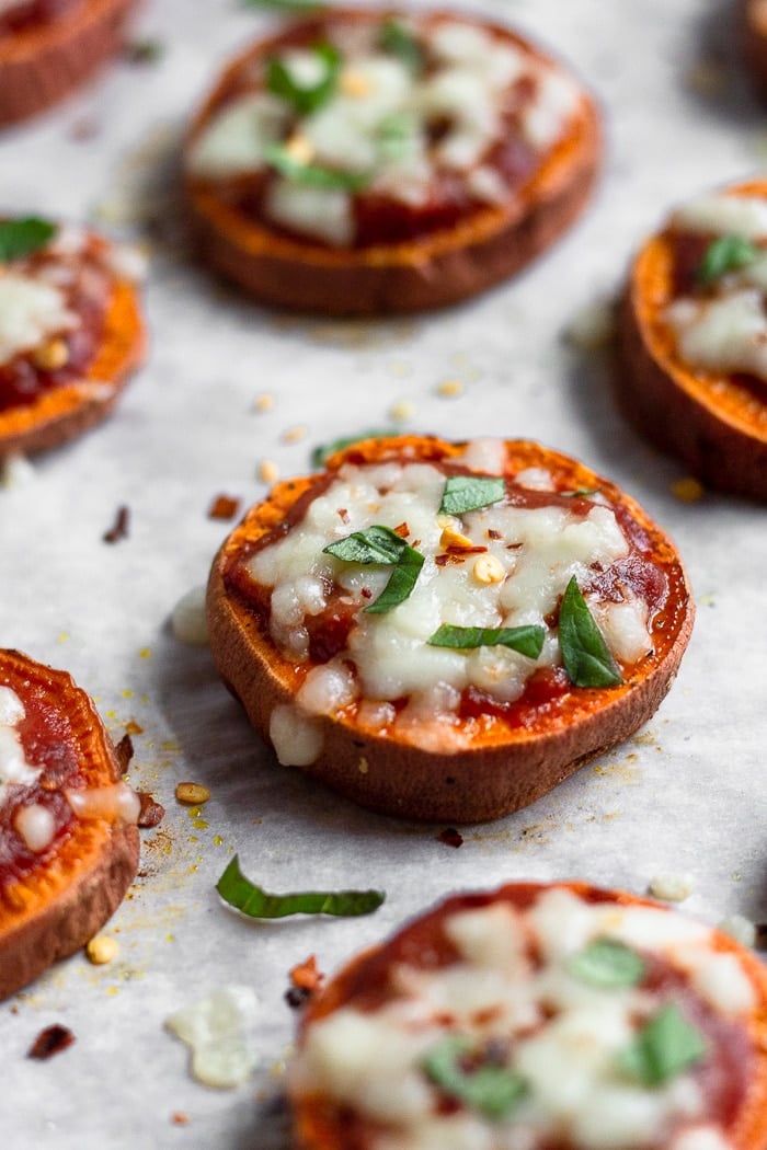 Parchment paper lined baking sheet filled with sweet potato pizza rounds topped with basil and red pepper flakes.