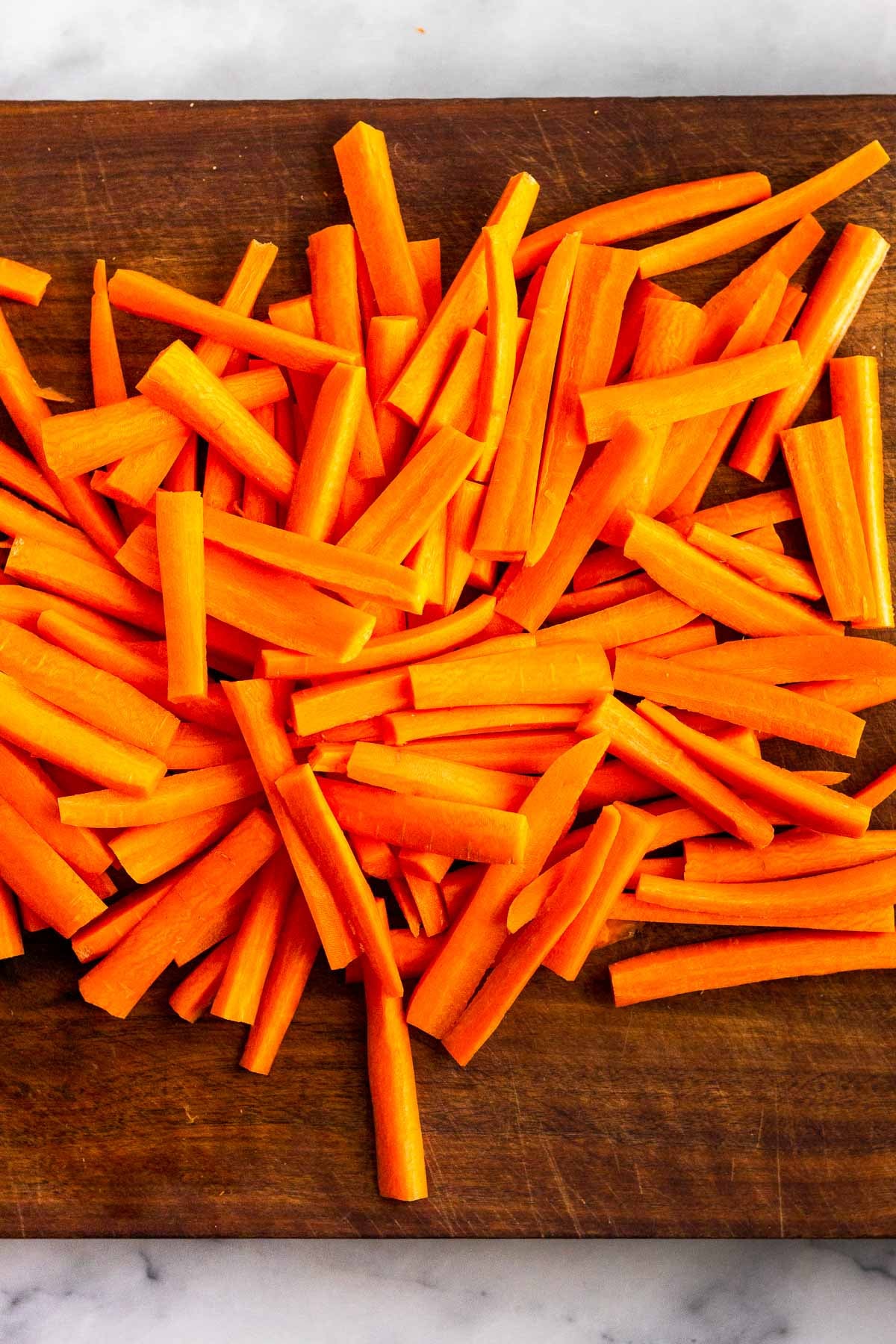 Cutting board with carrots cut into matchsticks on it.