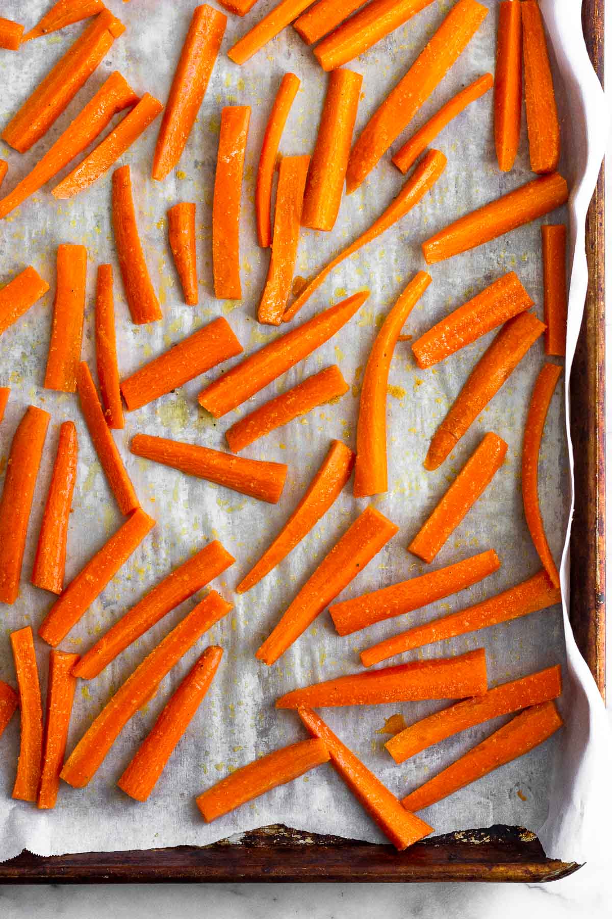 Baking sheet lined with parchment paper with matchstick carrots spread out across it.