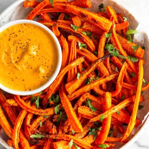Overhead shot of carrot fries in a bowl topped with cilantro. In the bowl is a small ramekin with curry dipping sauce.